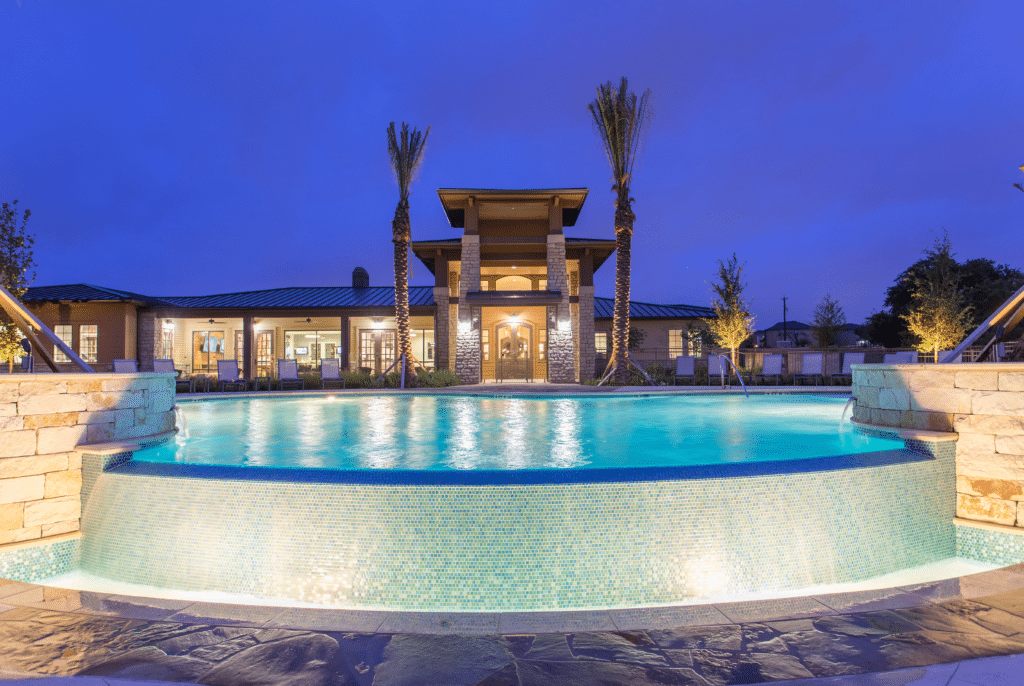 A nighttime view of a building with a lit pool in the foreground and a palm tree against the dark sky